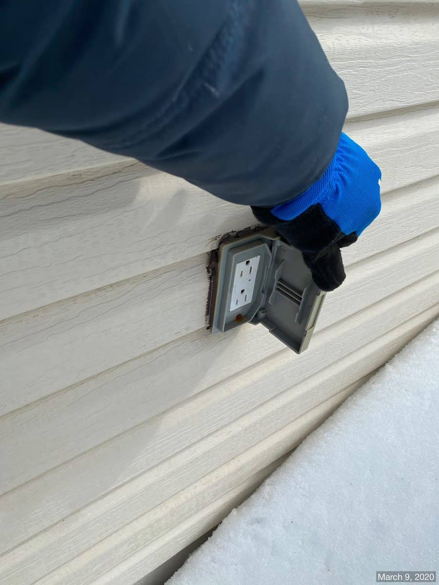 Issa checking an exterior outlet and siding penetration during an inspection